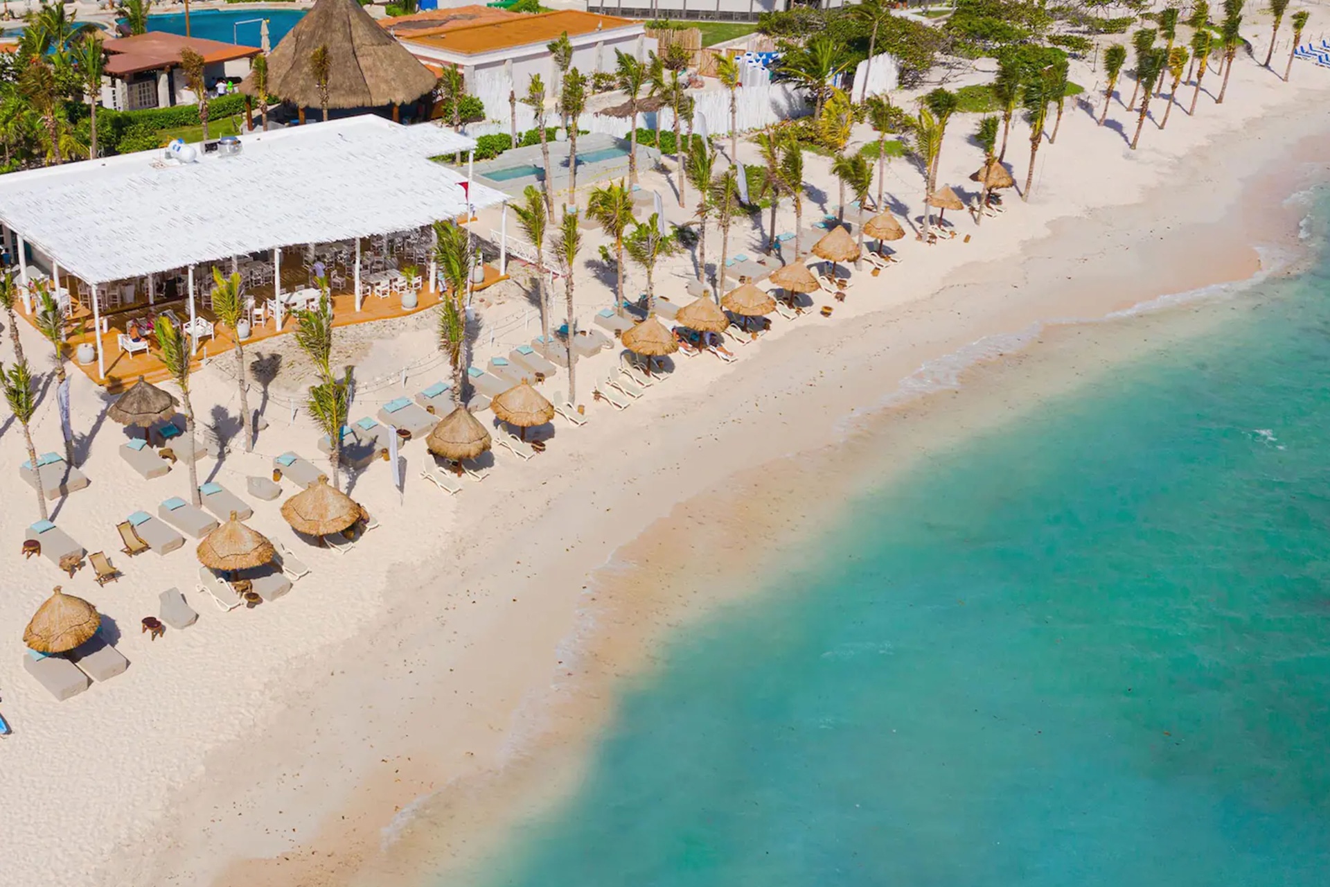 Aerial view of Kay Beach Club with white sand beach, palapas, and turquoise Caribbean water