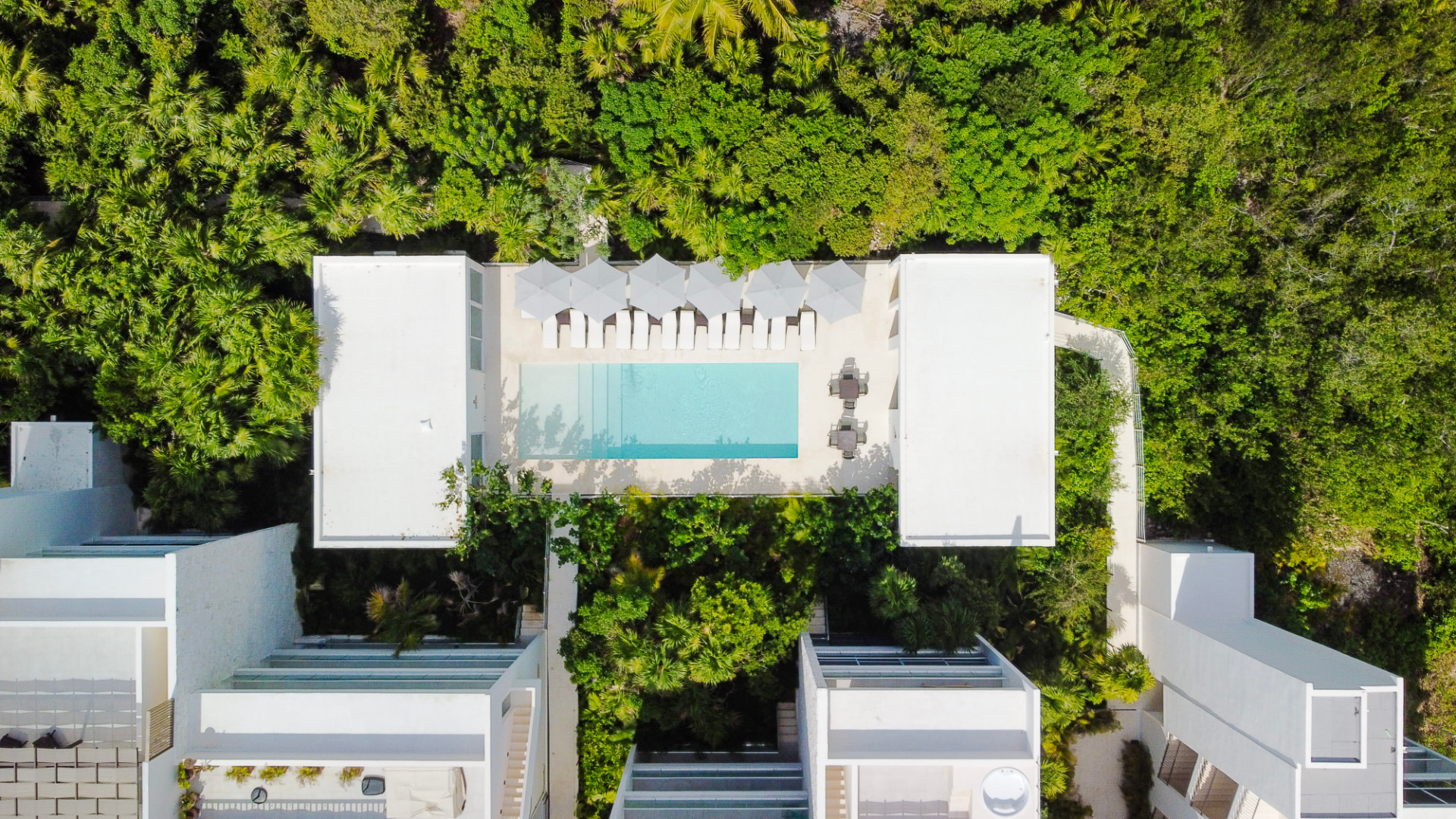 Overhead drone view of a Santamar by TAO pool with loungers and umbrellas surrounded by jungle