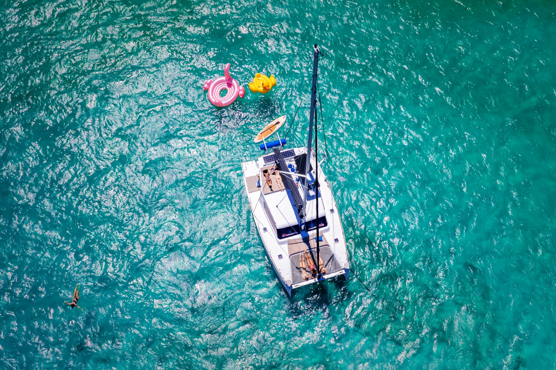 Aerial view of a luxury catamaran surrounded by turquoise Caribbean waters and inflatables in the Riviera Maya
