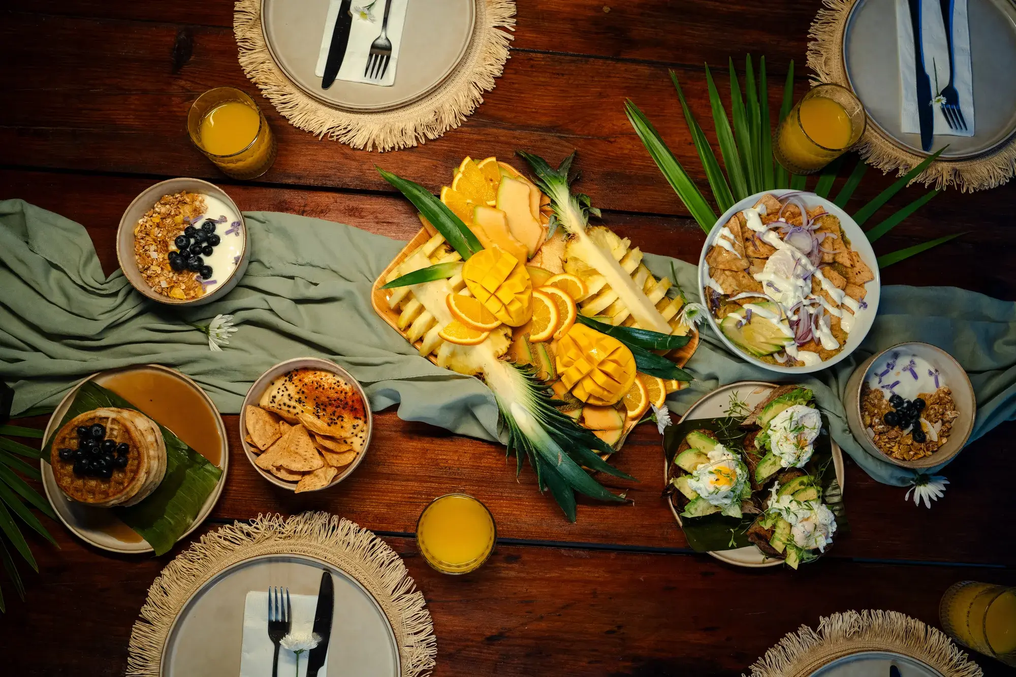Vista desde arriba de una mesa de desayuno tropical con fruta, waffles y bowls de yogurt