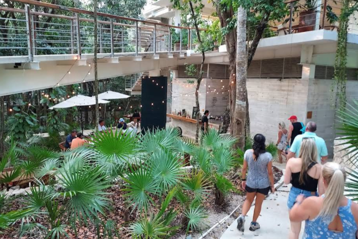 Open-air O'TAN Tulum restaurant surrounded by tropical palms, string lights and umbrella-shaded seating inside Tulum Country Club