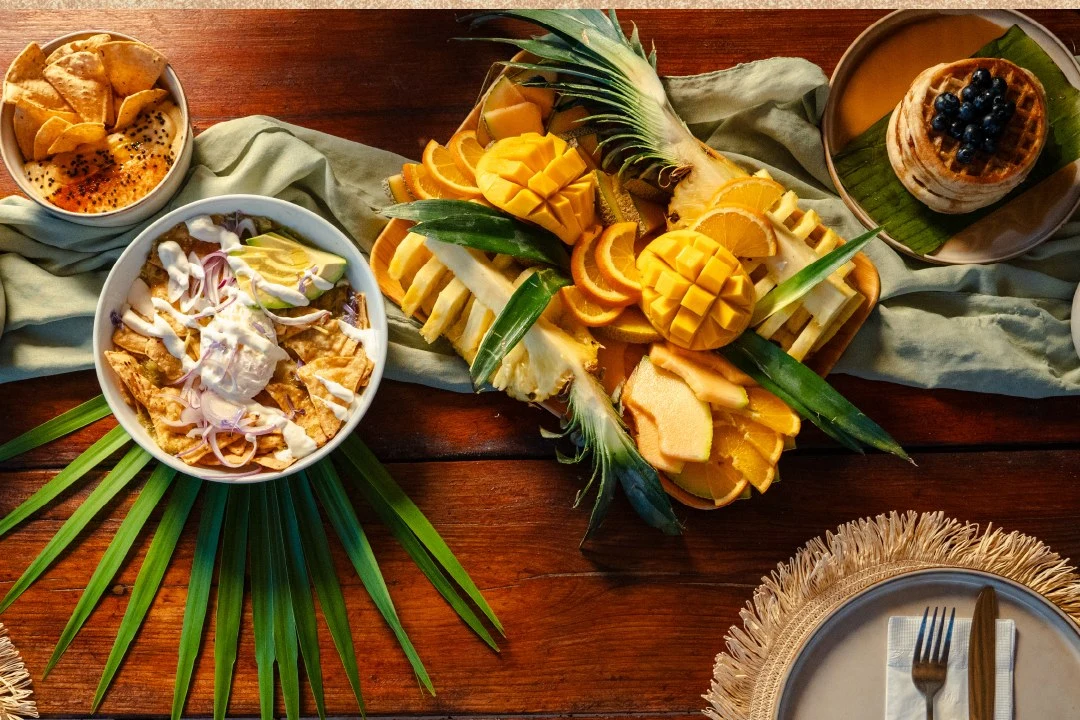 Fruta y platillos de desayuno en una mesa tropical
