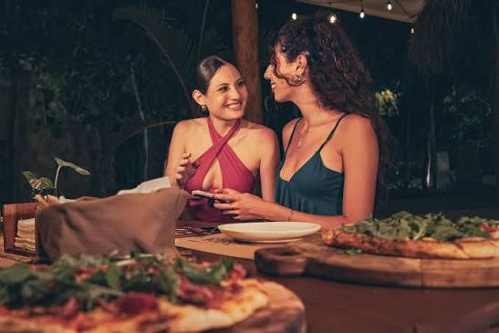 Two guests enjoying artisan pizzas and dinner in a warm, open-air restaurant setting at La Rústica
