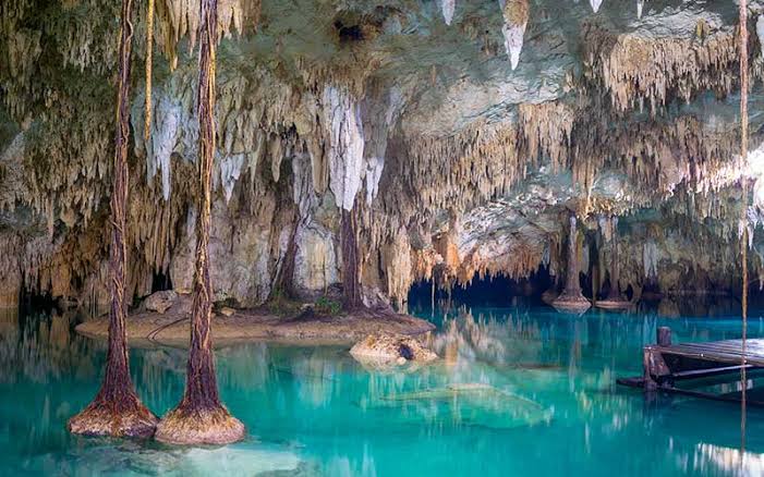 Crystal-clear turquoise water inside Sac Actun cenote cave with dramatic stalactites and hanging roots near Akumal