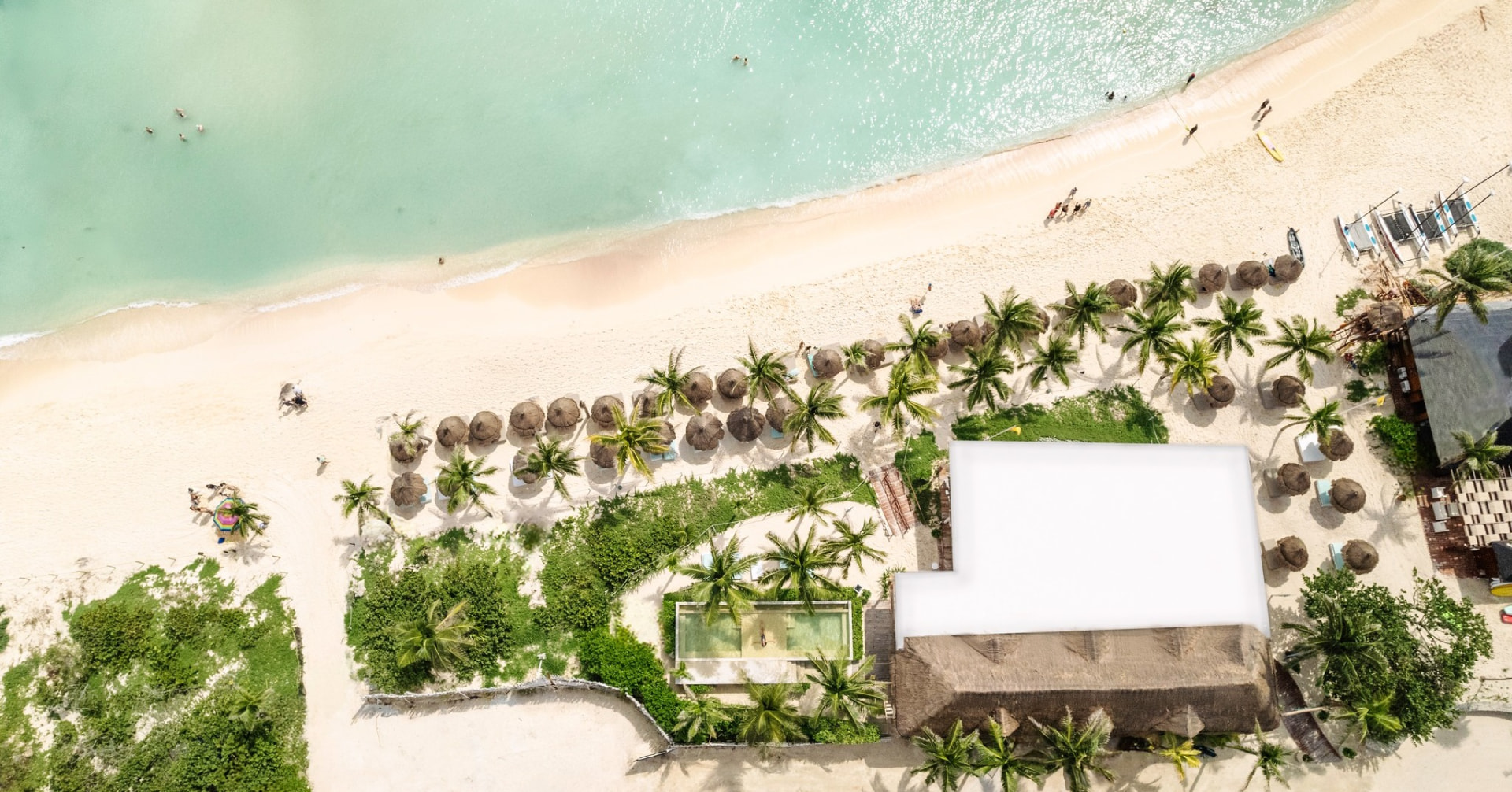 Overhead view of the white sand beach, palapas and turquoise water at the beach club used by Tulum Country Club guests