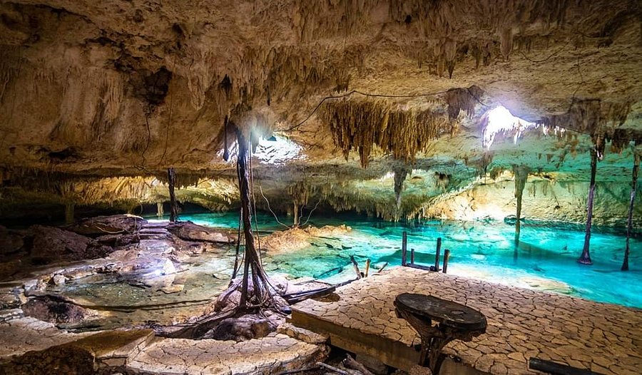 Crystal-clear turquoise water inside Taak Bi Ha cavern cenote, with limestone formations, stalactites and wooden walkways