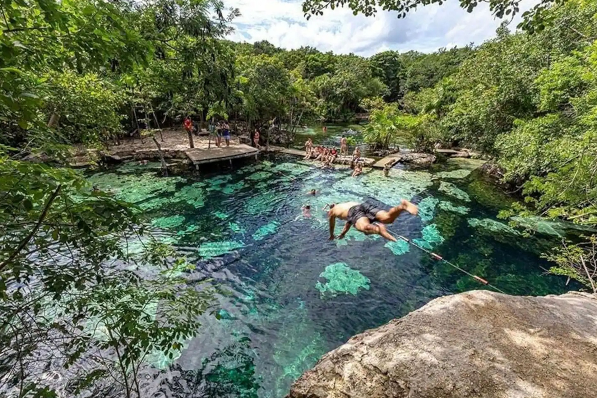 Person leaping into the vivid blue water of Cenote Azul