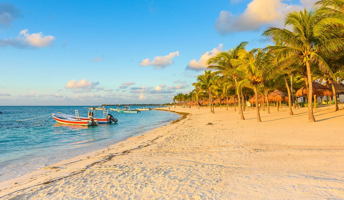 Sunrise over Akumal Beach with boats, palm trees, and thatched umbrellas along the sand