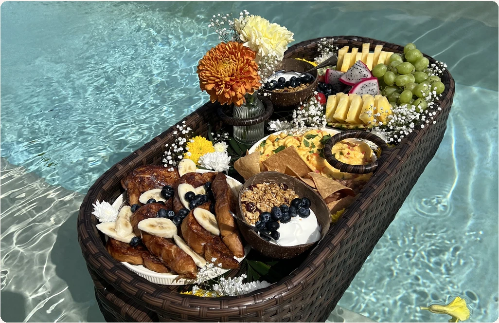 Charola de desayuno flotante con flores, fruta y platillos en una alberca