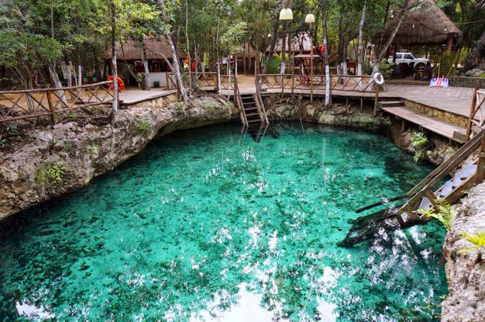Bright turquoise open cenote pool at Zacil-Ha with wooden walkways and jungle palapa near Akumal